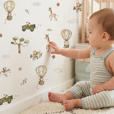 Bébé vêtu de bleu rayé blanc assis sur tapis et touchant mur décoré par stickers muraux cocon tendance