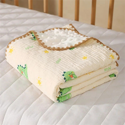 Couverture bébé Cocon Douceur large en mousseline et coton, motif dinosaures verts et étoiles, pliée sur le lit