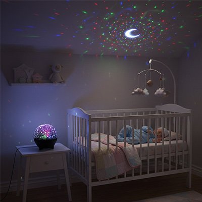 Bébé couché dans berceau dans chambre éclairée par veilleuse projection féérique