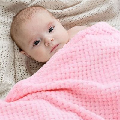 Bébé couché et éveillé couvert par Couverture bébé Douce Ecologique rose