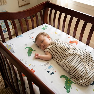 Bébé dans une gigoteuse blanche rayée de noir, sereinement endormi dans son berceau sur un matelas recouvert avec le drap housse lit bébé douceur plus