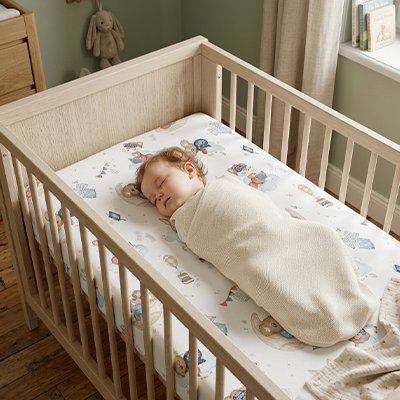 Bébé emmailloté dans une couverture beige, sereinement endormi dans son berceau sur un matelas recouvert avec le drap housse lit bébé douceur plus