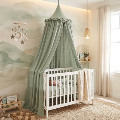 Bébé endormi dans son berceau blanc recouvert sur la longueur et décoré par le ciel de lit féerique vert
