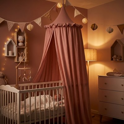 Bébé endormi dans son berceau décoré et recouvert sur la largeur par un ciel de lit atmosphère féerique rose