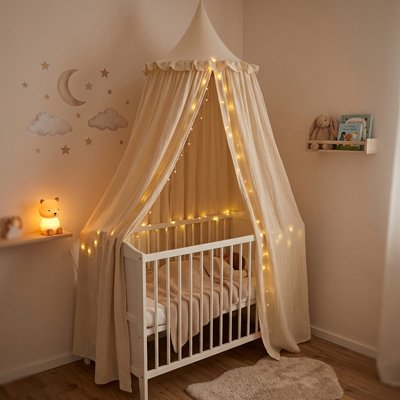 Bébé endormi dans son berceau décoré et recouvert sur la longueur par un ciel de lit atmosphère féerique beige