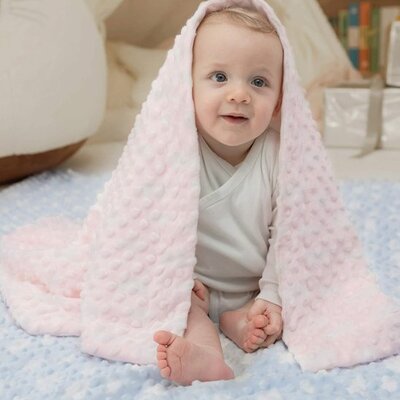 bebe pieds nus couvert par couverture bebe douceur nature rose et assis sur tapis bleu