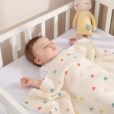 Bébé sereinement couché dans son berceau et recouvert avec la couverture bébé ultra-douce aux motifs cœur