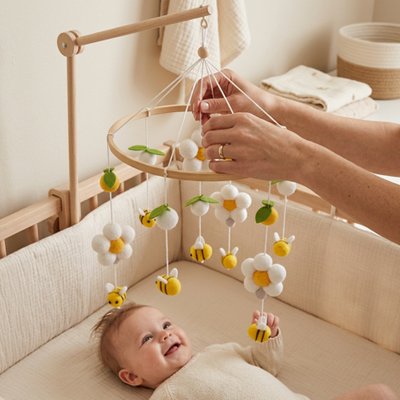 Bébé souriant dans son lit et regardant le mobile bébé apaisant musical suspendu au dessus de lui et réglé par des mains d'adulte