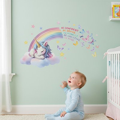 Bébé souriant et heureux assis sur le tapis dans la chambre décorée par stickers muraux enfant licorne motivante