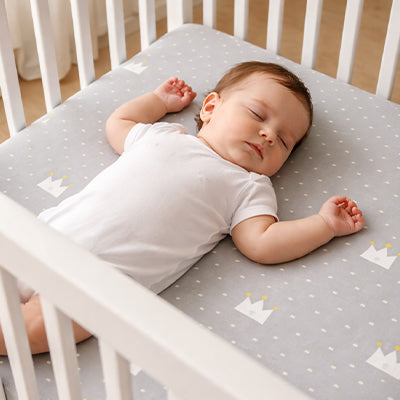 Bébé vêtu blanc cassé sereinement endormi dans son berceau sur un matelas recouvert par le drap housse lit bébé doux et respirant petites couronnes royales