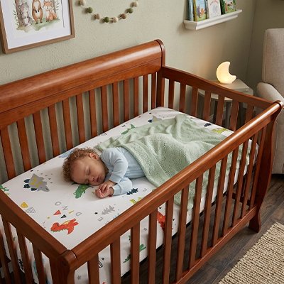 Bébé vêtu de bleu, mi-couvert, sereinement endormi dans son berceau sur un matelas recouvert avec le drap housse lit bébé douceur plus