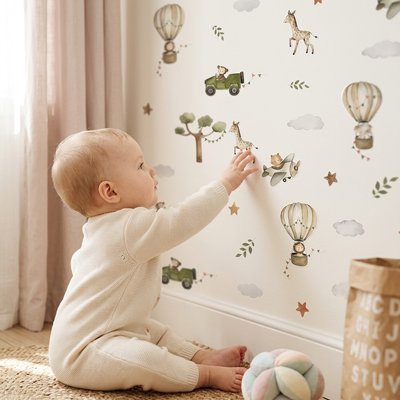 Bébé vêtu de beige assis sur tapis et touchant mur décoré par stickers muraux cocon tendance