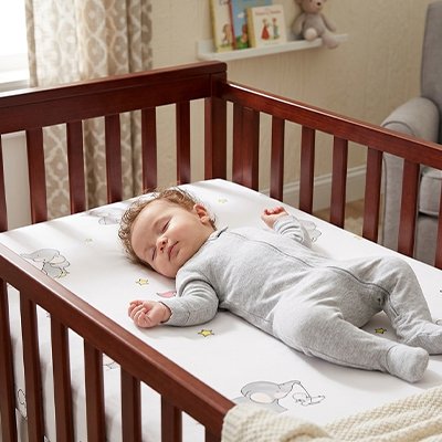 Bébé vêtu de gris sereinement endormi dans son berceau sur un matelas recouvert avec le drap housse lit bébé douceur et confort