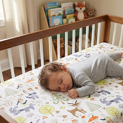 Bébé vêtu de gris sereinement endormi dans son berceau sur un matelas recouvert par le drap housse lit bébé doux et respirant forêt enchantée