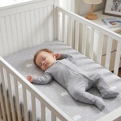 Bébé vêtu de gris sereinement endormi dans son berceau sur le matelas recouvert par le drap housse lit bébé doux et respirant petites couronnes royales