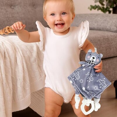 Bébé vêtu rose debout et heureux tenant Doudou Douceur Plus ours dans main gauche