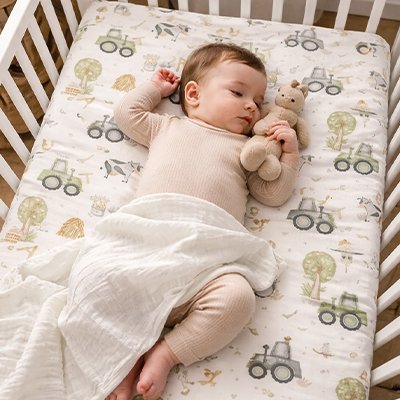 Bébé vêtu de rose et mi-couvert profondément endormi dans son berceau sur un matelas recouvert par le drap housse lit bébé douceur sécurisée
