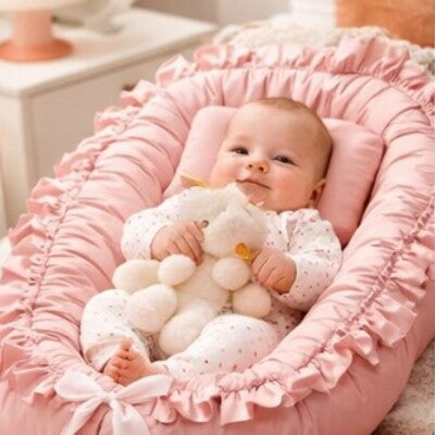 Bébé vêtu rose tenant doudou en mains couché sur dos dans nid d'ange bébé cocon rassurant