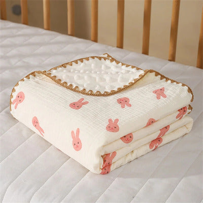 Couverture bébé Cocon Douceur large, extra douce, motif lapins roses, pliée sur un matelas de berceau blanc
