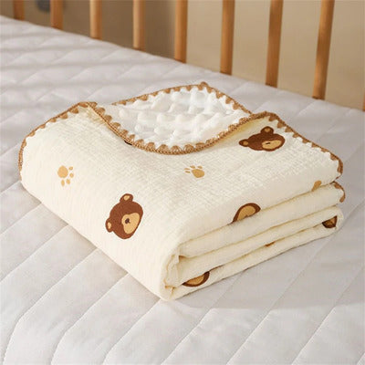 Couverture bébé Cocon Douceur en mousseline respirante, motif oursons marron et traces de pattes, pliée sur le lit