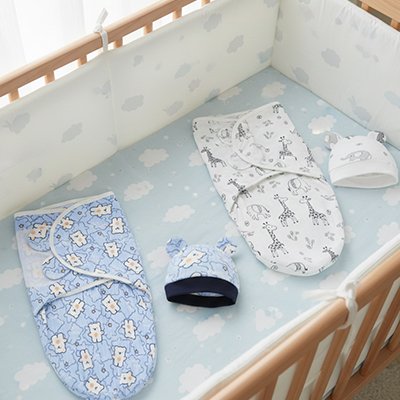 Deux couvertures emmaillotage Dodo Confort bleue et blanche étalées côte à côte sur matelas lit bébé blanc à barreaux