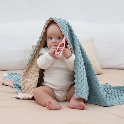 Enfant assis jouet en main recouvert par couverture bebe maxi epais bleu