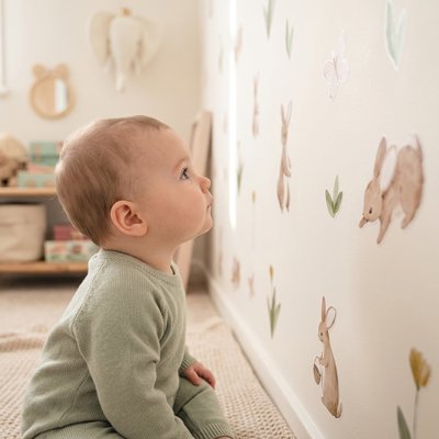 Enfant assis sur la natte séduit et attiré par décoration stickers muraux enfant univers apaisant