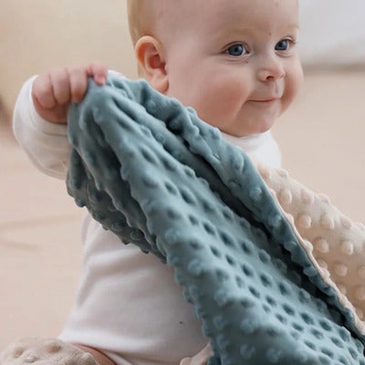 Enfant souriant assis jouant avec couverture bébé Maxi Epais bleu