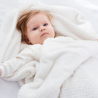 Fillette couchée et éveillée enveloppée dans Couverture bébé Douce Ecologique blanche