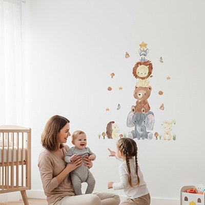 Maman assise tenant bébé et communiant avec sa fille dans chambre décorée par stickers muraux enfant animaux aventuriers