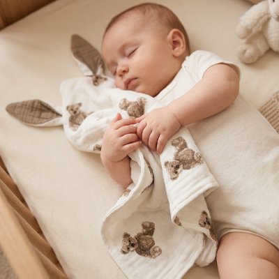 Vue de face de bébé endormi avec doudou confident rassurant ourson assis dans les bras