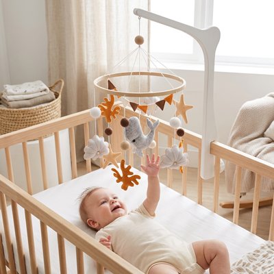 Vue profil de bébé souriant couché sur le dos dans son lit et touchant de la main le mobile bébé apaisant baleine blanche suspendu sur le lit