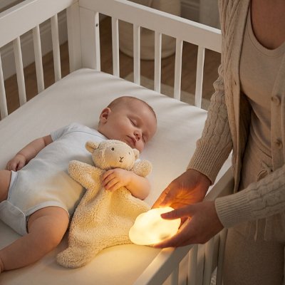 Vue profil droit de bébé endormi avec doudou bébé compagnon fidèle dans bras et mère debout tenant veilleuse