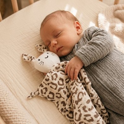 Vue profil droit bébé profondément endormi avec doudou bébé compagnon doux léopard dans bras