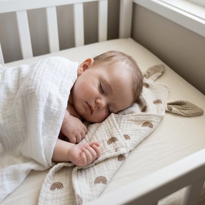 Vue profil droit bébé sereinement endormi avec doudou premier câlin beige dans bras