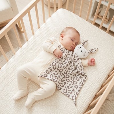 Vue profil gauche bébé profondément endormi avec doudou bébé compagnon doux léopard dans bras