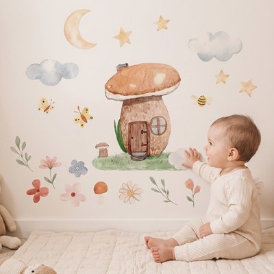 Vue profil gauche bébé vêtu beige assis touchant de main mur orné par stickers muraux chambre déco raffinée
