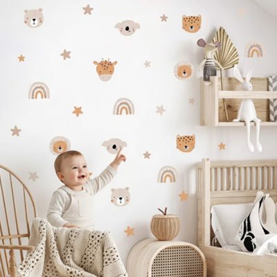 Vue profil gauche de bébé debout et pointant mur décoré avec stickers muraux enfant savane douce