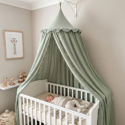 Zoom avant de bébé endormi dans son berceau blanc recouvert sur la longueur et-décoré par ciel de lit féerique vert